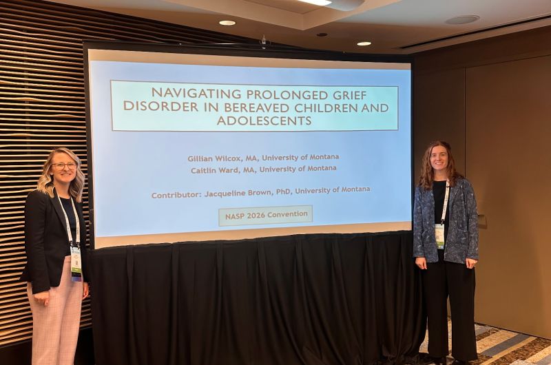 Two graduate students, Gillian and Caitlin, standing in front of a screen at a conference presentation