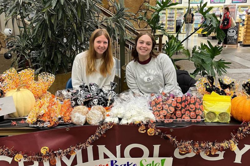 Crim Club students sitting at a table full of bake sale treats to raise money.