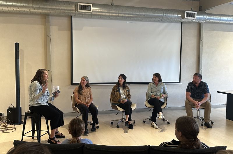 four professors participate in a panel discussion in front of a large projector screen