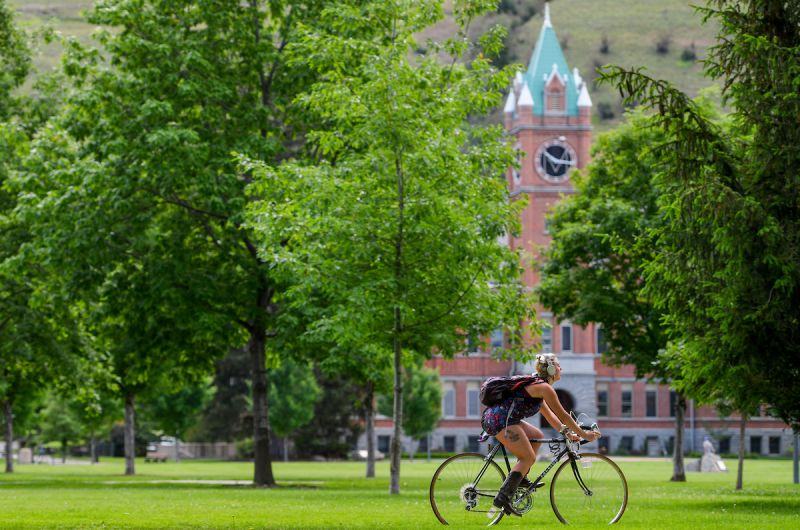 girl riding bike through green campus