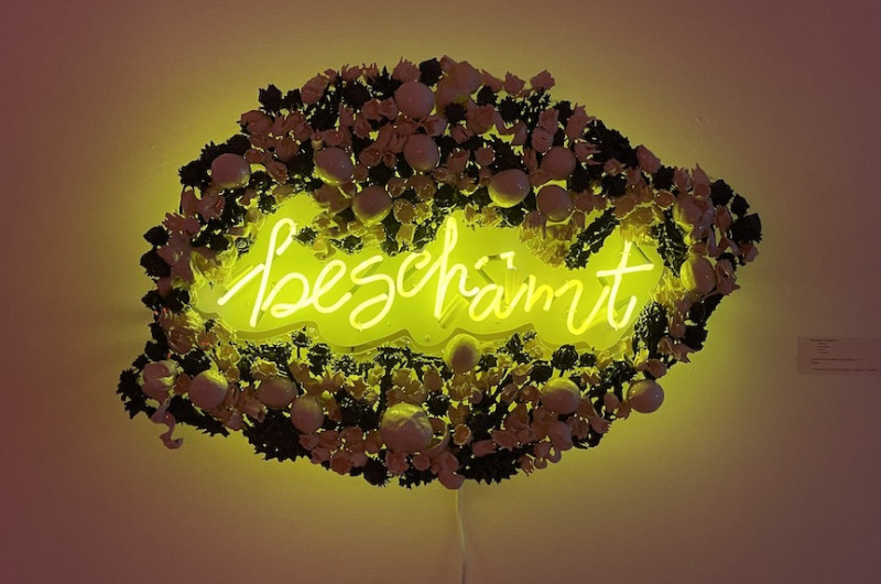 neon art with ceramic frame, neon is yellow and says 'beschamt,' frame is in the shape of a lemon made of ceramic lemons and flowers
