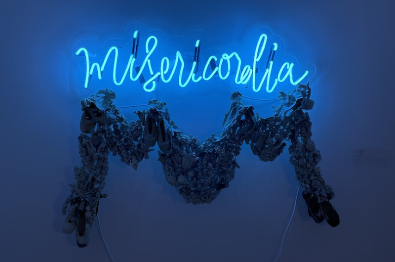 neon sign in cursive 'misericordia' with a ceramic garland below, blue
