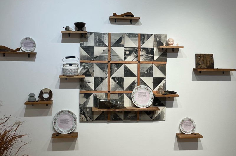 center is a wooden 'quilt' made from cutup old photographs, with shelves on and surrounding it, featuring various found objects, ceramic plates with poems, a jar of dirt, and rusted junk