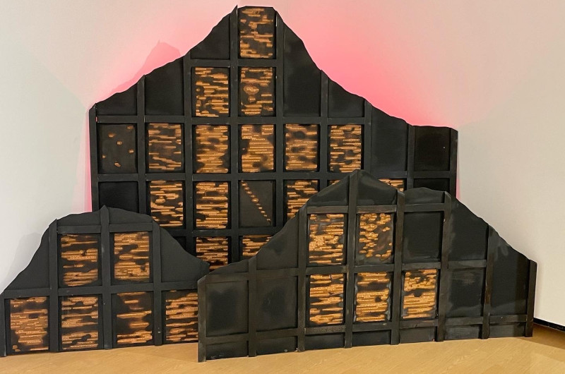 wooden mountain forms with grids, poems are etched into grids much like stained glass windows. three mountains are backlit with red light