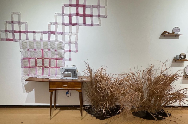 left to right: pink and purple paper quilt in honeycomb shape on wall, vintage sewing machine, dried grasses and dirt