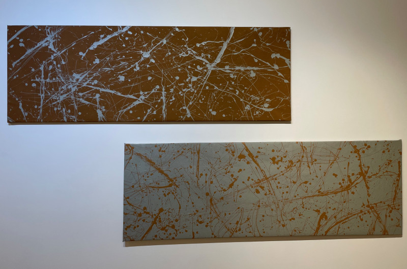 two abstract paintings hanging horizontal, top is brown background with silver paint, bottom is silver with brown paint
