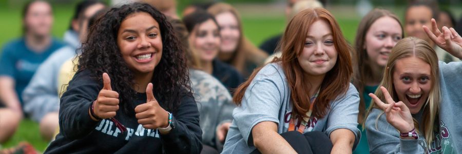 group of students sitting outside on the grass posing and making hand gestures to the camera