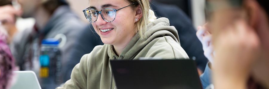 student smiling and looking at a laptop in a group of other students