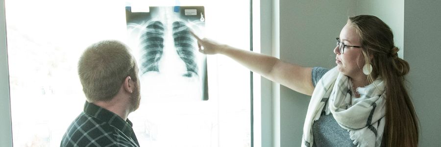 two people looking at an xray in a lightbox with one person pointing out things