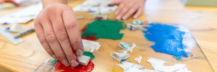 close up view of a hand mixing paint on a piece of glass