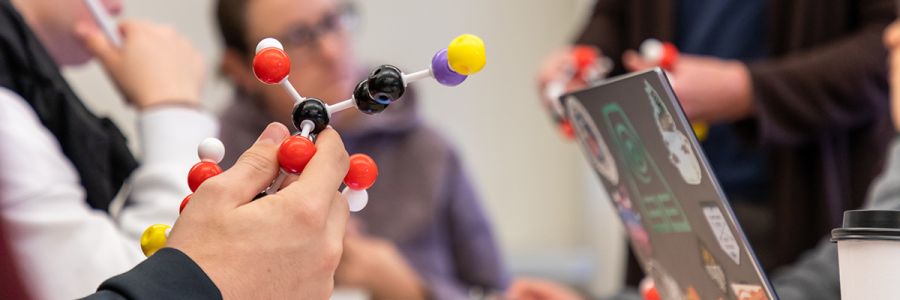 hand holding a model of a molecule with other students in the background