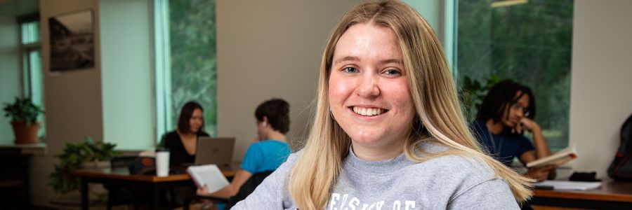 student smiling for the camera with students studying at tables in the background