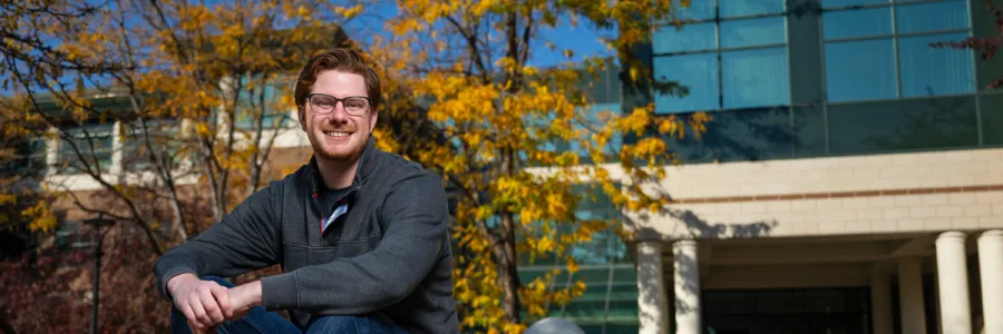 A Business student sits for a portrait outside the Gallagher Business Building on the University of Montana campus on a fall day.