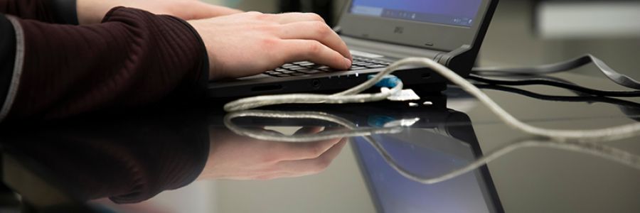 close up view of hands typing on a laptop that is hooked up with various wires