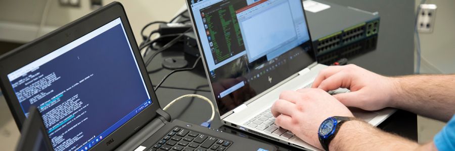 hands typing on a laptop with another open laptop and other networking equipment on the table