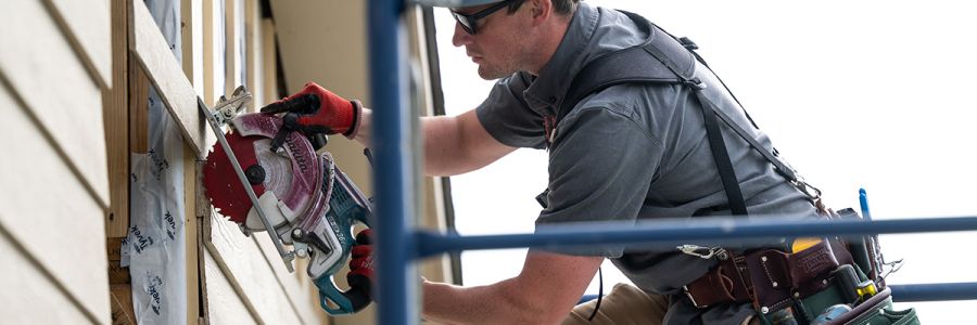person wearing safety gear standing on scaffolding using a circular saw