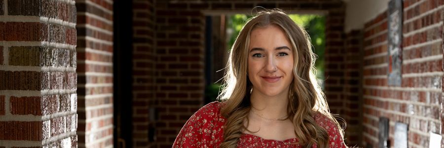 student smiling for camera in a brick lined outdoor hallway