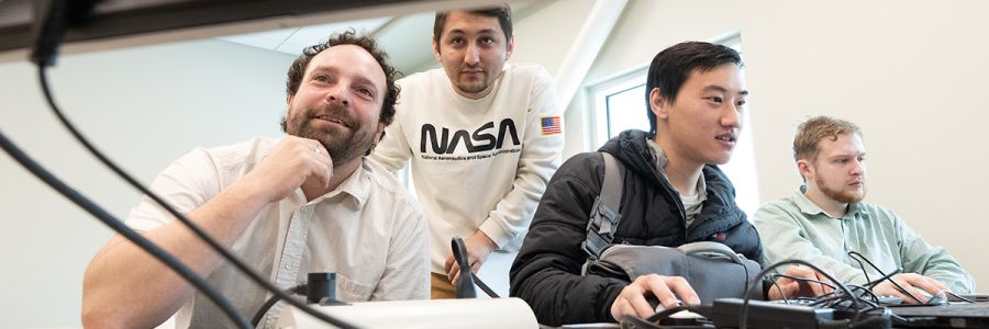 row of three people working at computers while another looks on from behind