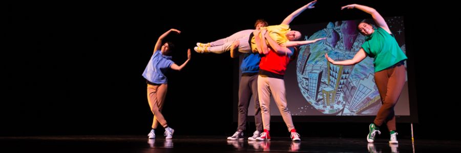 two students holding one up horizontally while two other students bend and point their hands at either side of them