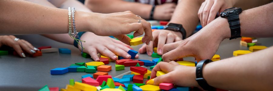 close up view of several peoples hands grabbing and working with a pile of brightly colored toy blocks