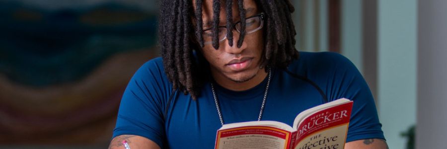 student sitting and reading a book with one hand while taking notes with a pencil in the other hand