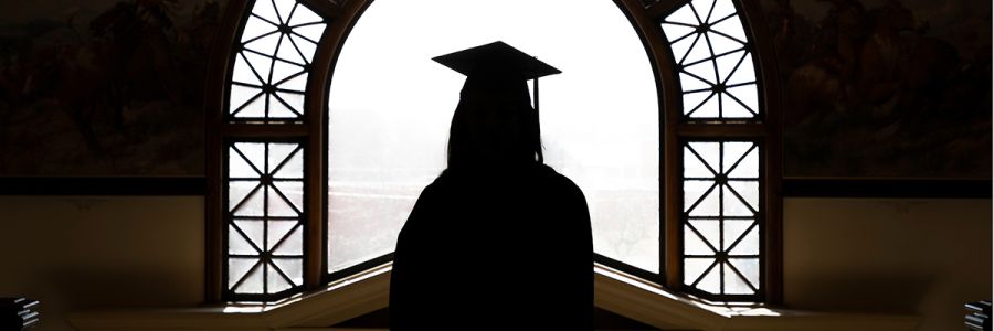 silhouette of a person in graduation garb in front of a bright window