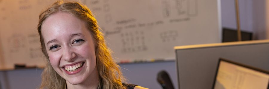 smiling student in front of a whiteboard filled with writing and figures