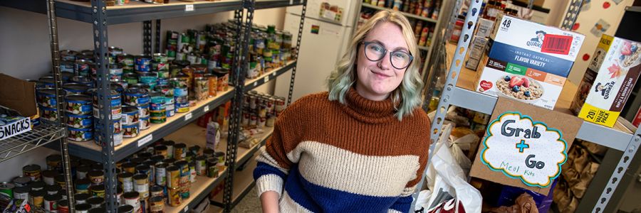 headshot of UM staff in the UM food bank with shelves full of canned 