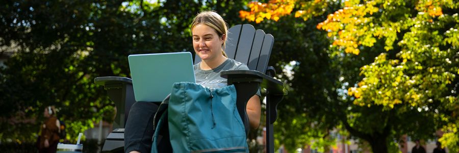 smiling student sitting outside in a chair working on their laptop