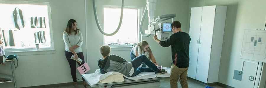 four people in an exam room with one on a bed and others using x-ray equipment