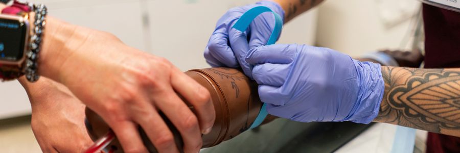 close up view of two sets of hands practicing nursing on a training dummy arm