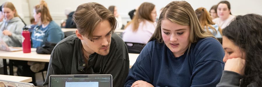 group of students in a classroom working in a group with other groups in the background
