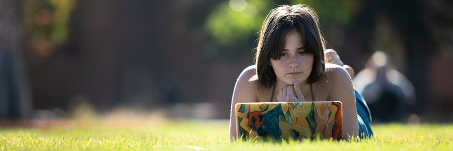 student looking at a laptop while laying in the grass on a sunny day