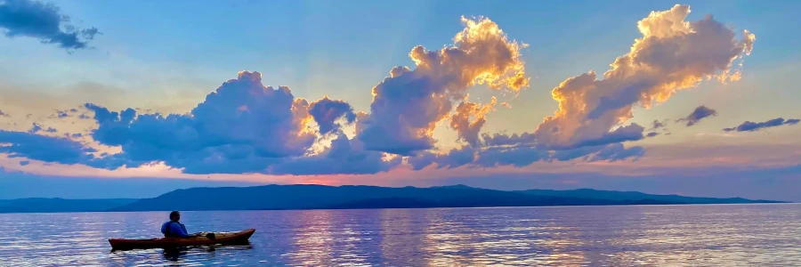 kayaker floating on a lake with mountains and a dramatic cloud filled sky in the background reflected on the lake