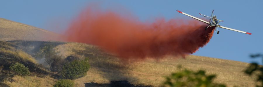 small plane flying low down a mountain while release a cloud of red fire retardant 