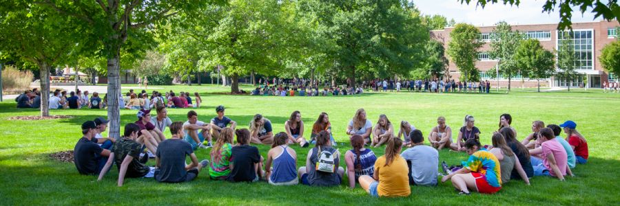 large groups of students sitting outside on the ground in circles on the UM campus
