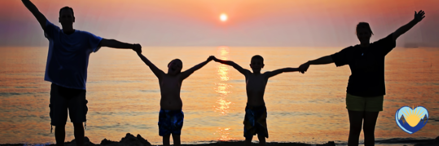 two adults holding hands with two kids in the middle on a beach at sunset