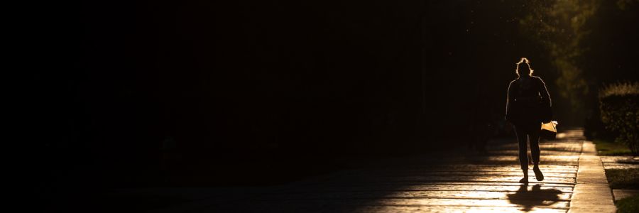 person walking on campus in the dark highlighted in orange light