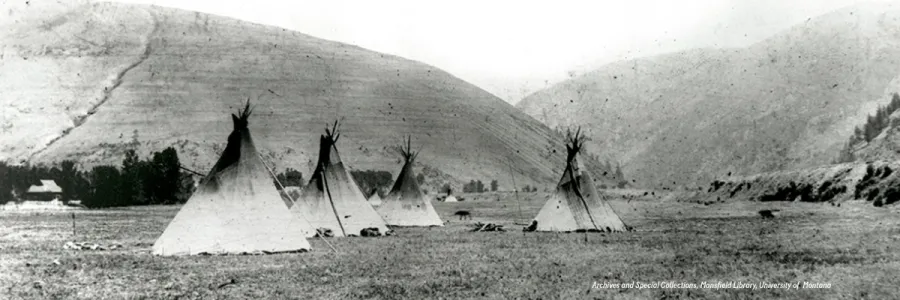 Indian tents (tipis) pitched in front of Hell Gate Canyon, area where Missoula, Montana, is now situated. Mount Jumbo and Mount Sentinel on either side. Photo credit text in bottom right corner "Archives and Special Collections, Mansfield Library, University of Montana".