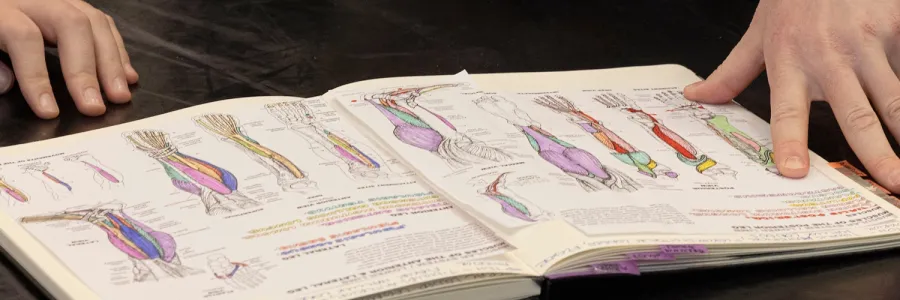 Two students consult an anatomy book during a class at UM
