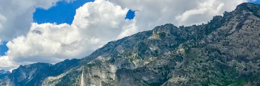 rocky, tree covered mountain with cloudy blue sky above