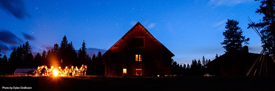 people around a campfire in front of a cabin at night
