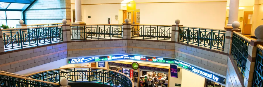 View of the Gallagher college of business building atrium featuring a multi-level design with decorative railings and digital signage displaying stock information