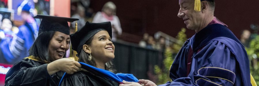 student at a graduation ceremony having a sash put on them by two people