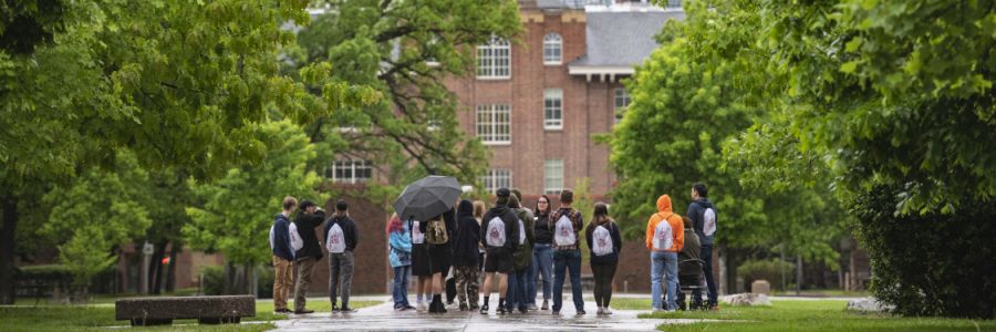 students standing in a group on a walking path at the university in the rain