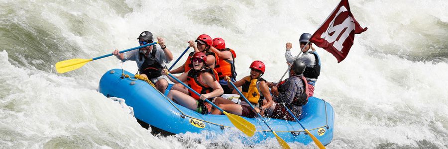 group of people white water rafting while flying the UM flag