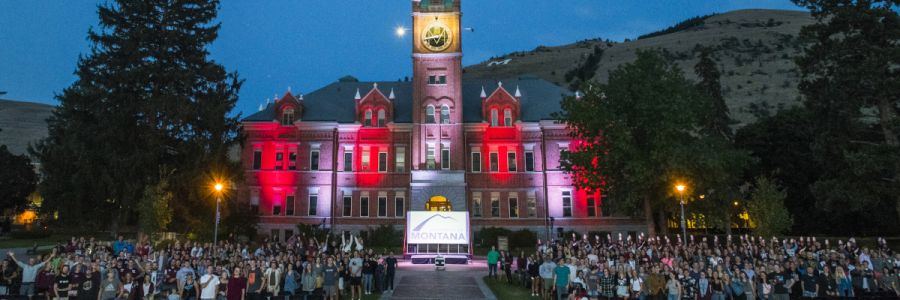 large group of people attending an event on the oval in front of University Hall lit up with red and pink lights
