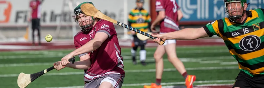 Griz hurling player swings at a ball as a defender covers the player