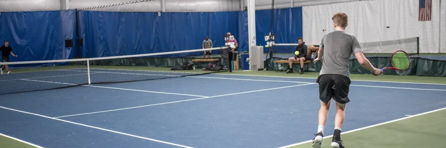 Two Griz club tennis players volley on an indoors court