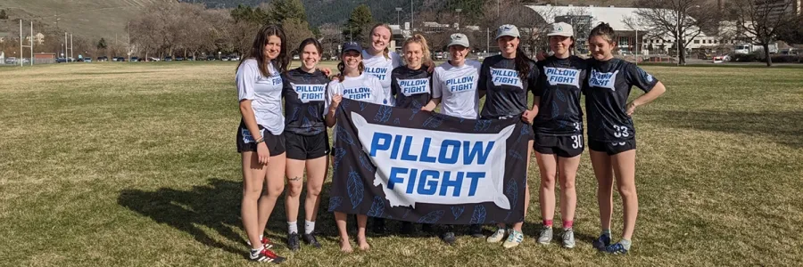 Members of UM's women's ultimate frisbee team stand for a photo while holding a flag that reads "Pillow Fight"
